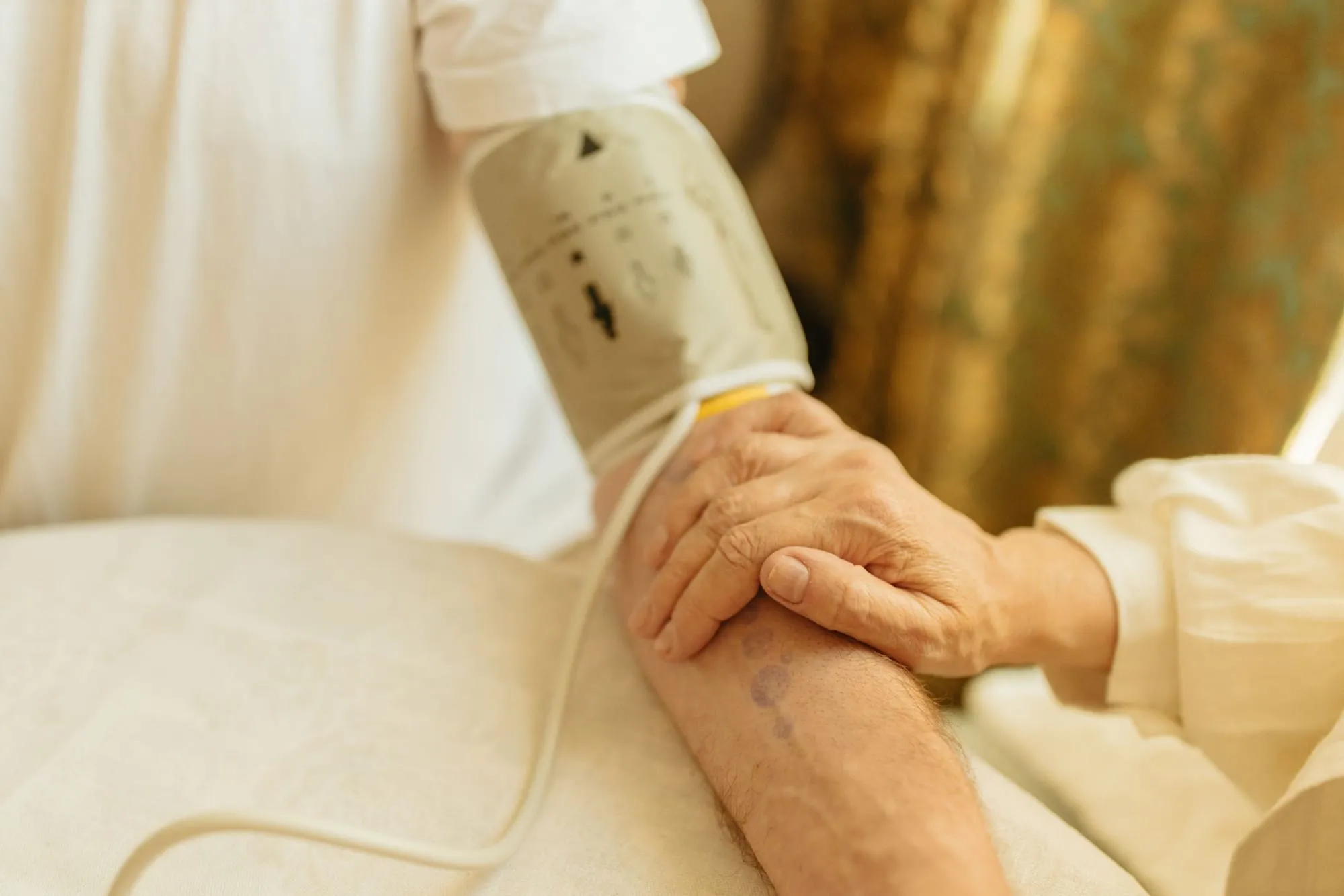 Blutdruckmanschette am Arm einer älteren Person, zu Hause am Tisch