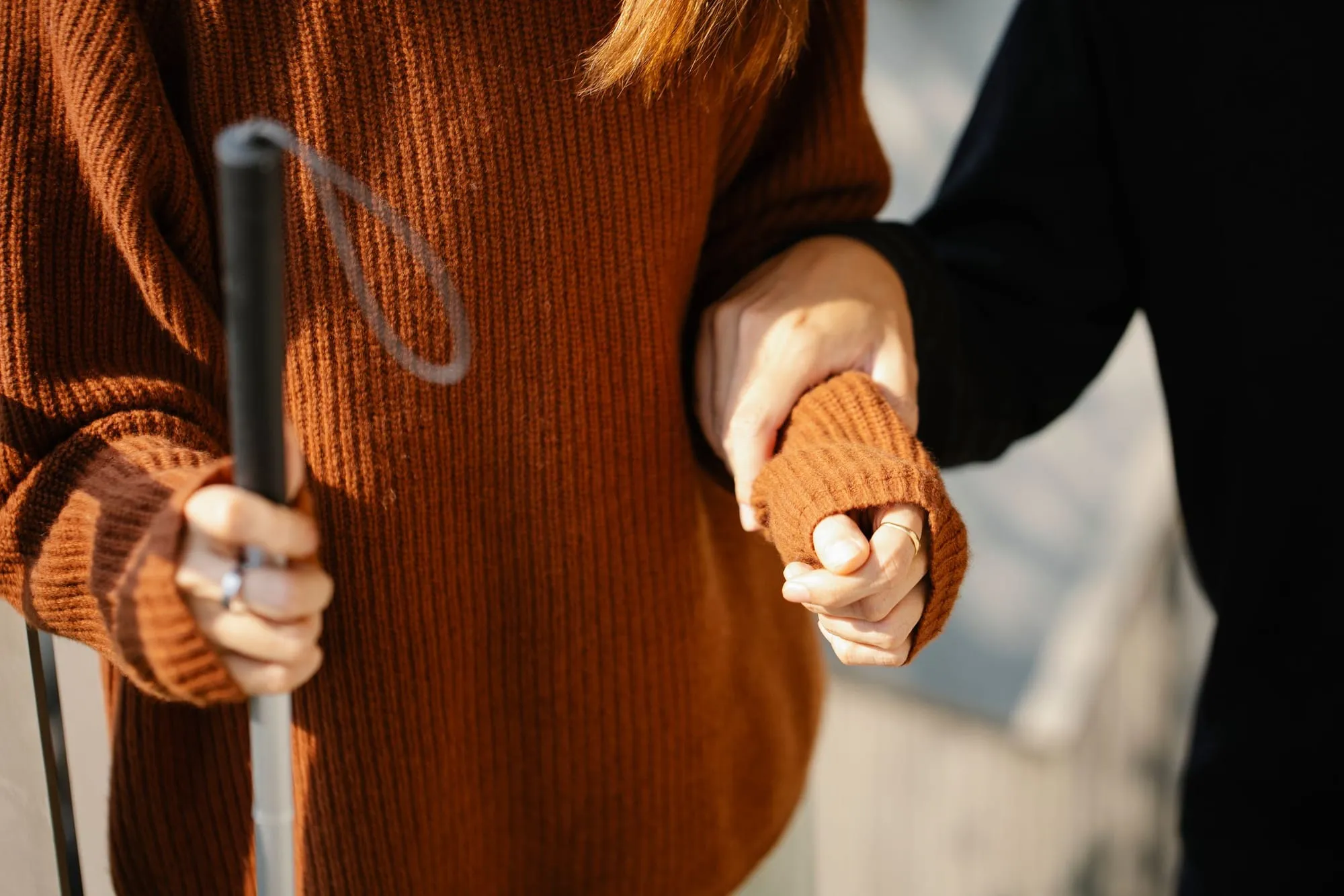 Eine Hand stützt eine ältere Person mit Gehstock am Arm