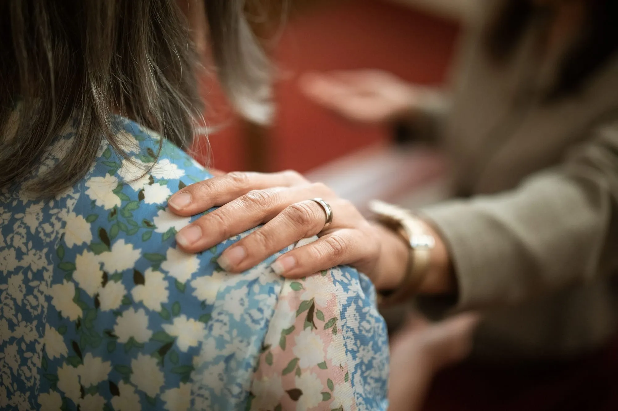Eine Hand liegt tröstend auf der Schulter einer älteren Frau